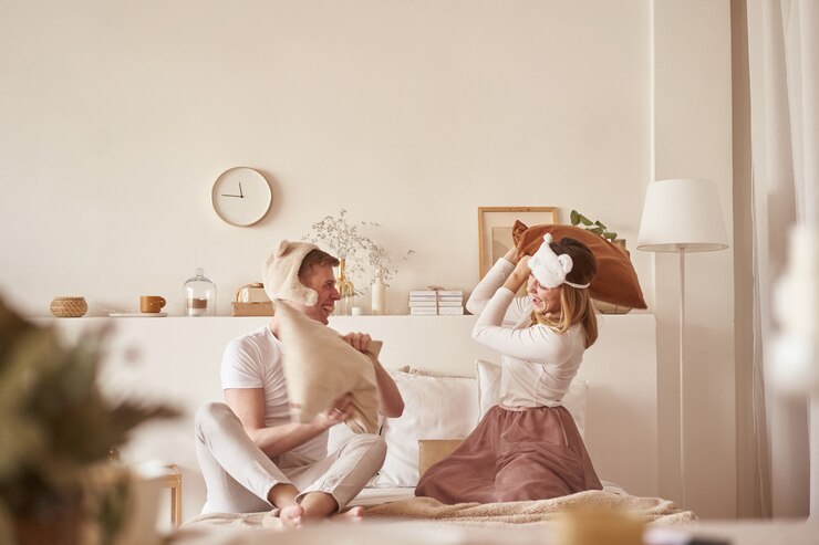 Pair in love laughing and playing on bed. Man and woman fight pillows. Young happy couple beat the pillows on the bed in a bedroom at home