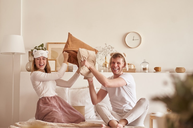 Pair in love laughing and playing on bed. Man and woman fight pillows. Young happy couple beat the pillows on the bed in a bedroom at home