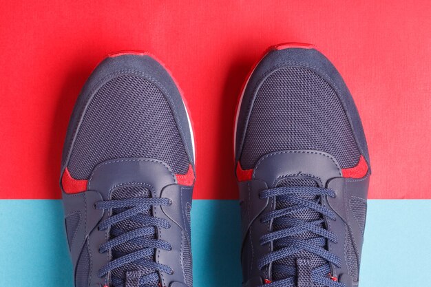 Pair of mans sport sneakers on blue and red background.