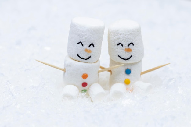 A pair of marshmallow snowmen sit in the snow.