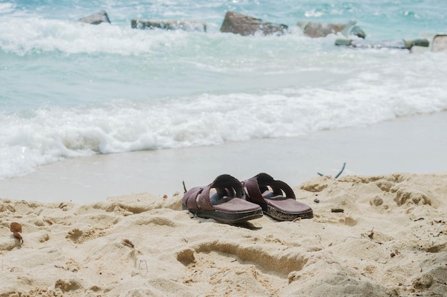 Foto coppia di sandali da uomo nella sabbia di fronte alla spiaggia onde del mare sullo sfondo