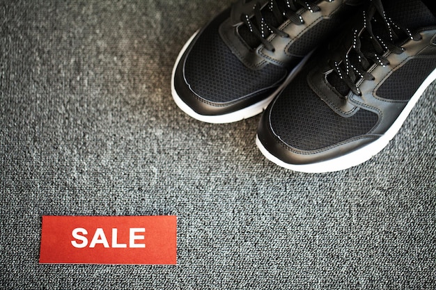 Pair of new stylish black sneakers with discount on gray background.