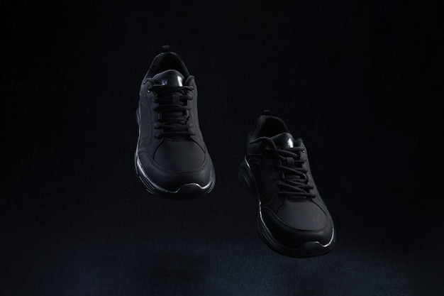 Фото Пара черных кроссовок других производителей, летящих на темном фоне. черные спортивные кроссовки парят в воздухе.
