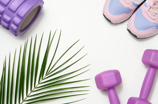 Pair of pink sneakers and purple dumbbells on a white
background, sports. copy space