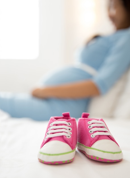 A pair of pink toddler sneakers beside a pregnant woman