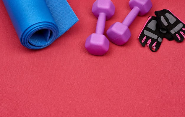 Pair of purple plastic dumbbell, gloves and a blue sports mat on a red 