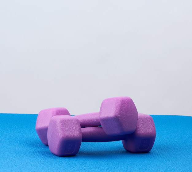 Пара фиолетовых пластиковых гантелей для занятий спортом на синем коврике