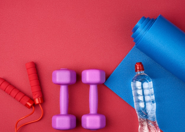 Pair of purple plastic dumbbells, bottle of water  on a red neoprene mat