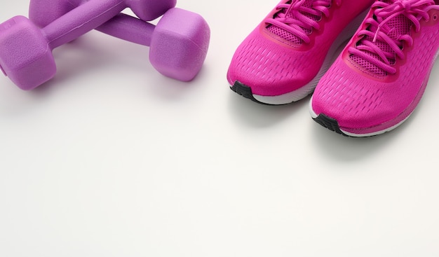 Pair of purple sneakers, plastic dumbbell on a white background, top view, copy space