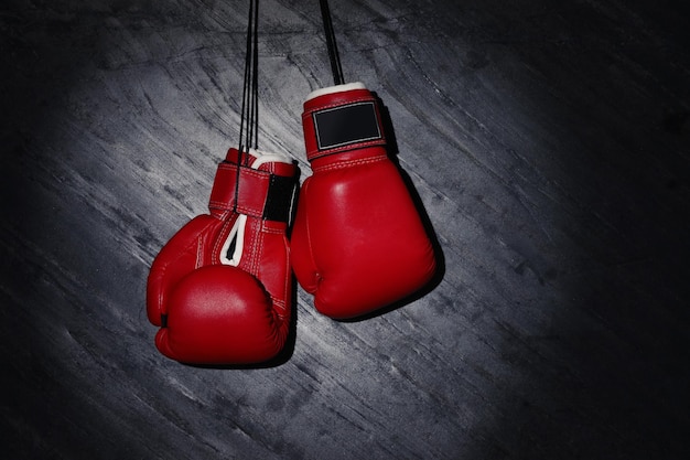Pair of red boxing gloves hanging in spotlight on grey stone background Space for text