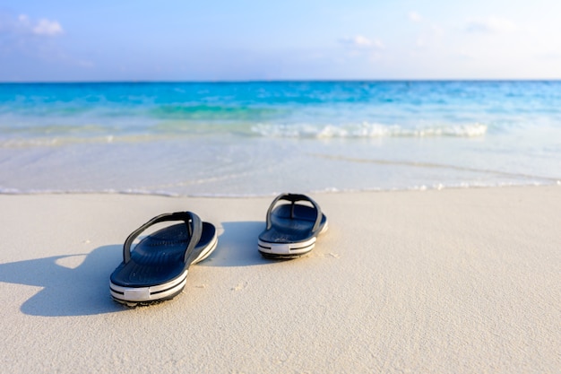 Foto paio di scarpe sandali sulla spiaggia di sabbia bianca.