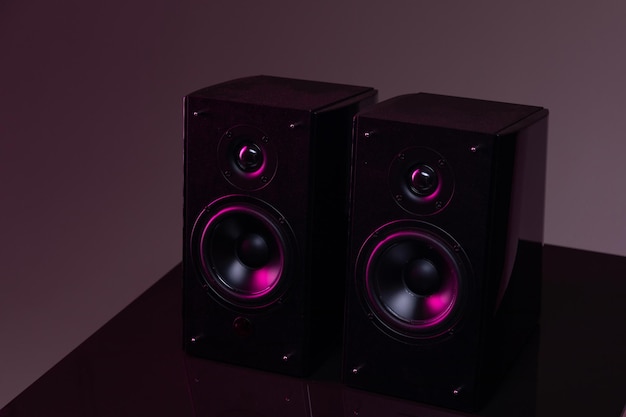 A pair of speakers for listening to music on a dark background with purplelilac backlighting