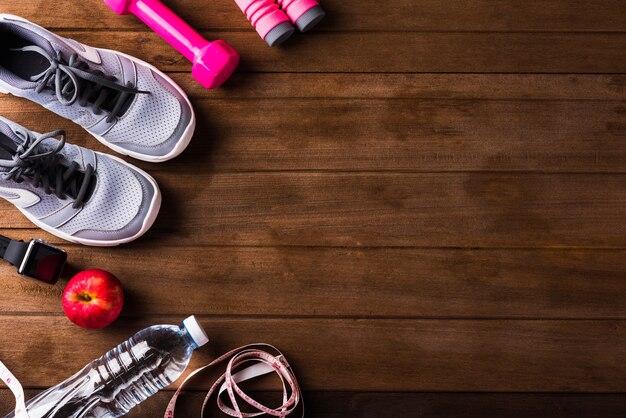 Pair sports shoes, apple, jump rope and dumbbell on wood table