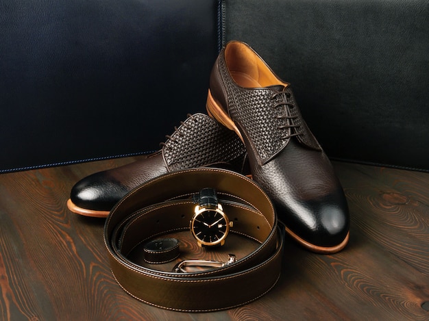 A pair of stylish leather shoes lies next to a brown leather belt, side view, close-up