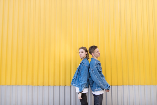 Pair of stylish people standing backs against background of yellow wall. Hipsters photo.