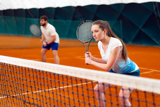 Pair of tennis players, man and woman waiting for service at indoor court