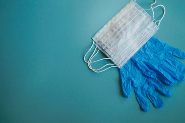 A pair of thin blue medical latex gloves and a protective mask on a blue background