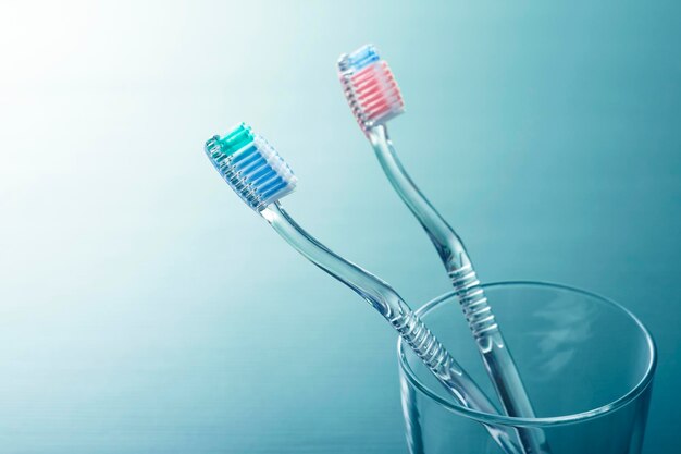 A pair of transparent plastic toothbrushes in a glass