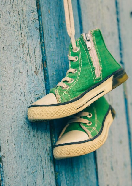 Pair of used green textile shoes hang on a blue background close up