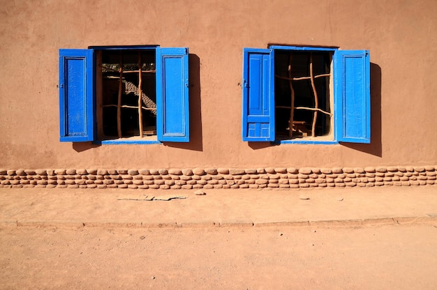 Pair of vivid blue colored wooden windows on brown adobe facade in the sunlight