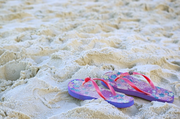Pair of vivid colored flip-flops sandals on the sandy beach