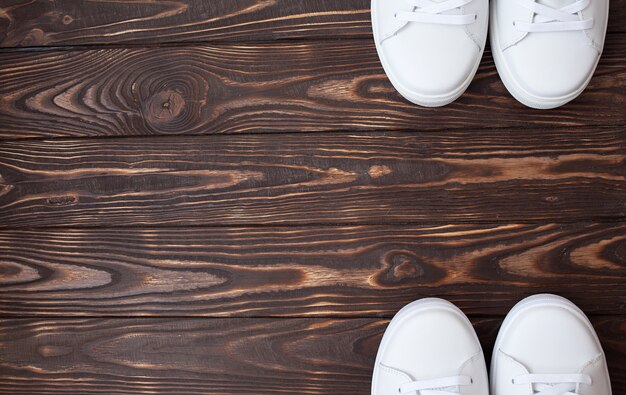 A pair of white canvas shoes on a wooden. White sneakers on brown background.