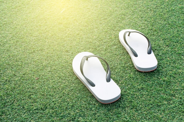 Pair of white flip flops in green grass background with burst sunrise light ,dream soft style