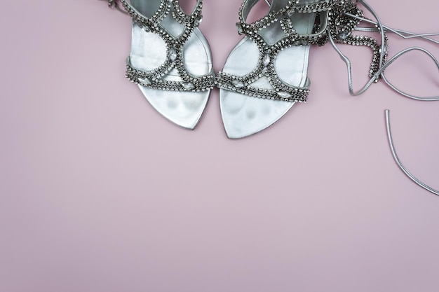 A pair of white sandals with silver beads on a pink background.