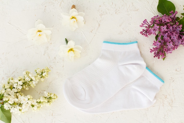Pair of women socks, lilac flowers, jasmine flowers and buds of\
daffodil flowers on the white structured background, top view.