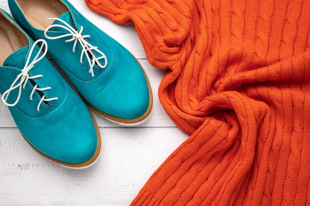 Pair of womens aqua oxfords and orange pullover on white wooden background. Flat lay, casual trendy style concept. Fashion clothes.