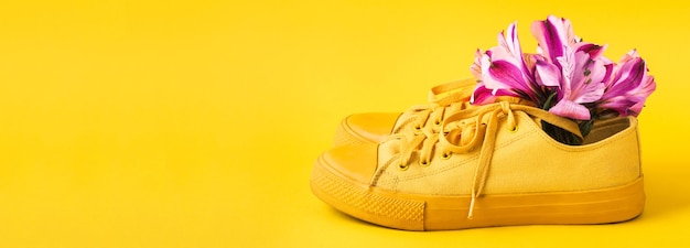 Pair of yellow sneakers and flower buds on yellow banner Spring summer fashion concept front view copy space