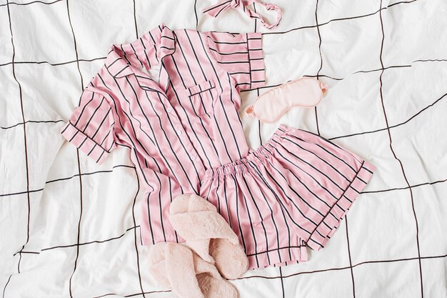 Pajamas sleeping kit with fluffy fur slippers. Classic pink sleep dress with stripes in bed. Good morning concept. Flat lay, top view