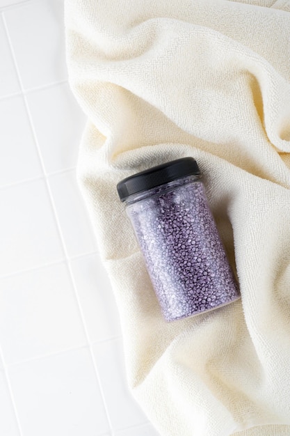 Pakket van paars glanzend kristalzout op een beige badkamerhanddoek Pot met glinsterend paars zeezout voor thuisspa Idee van ontspanning, aromatherapie en zelfzorg Het effect van zeewater op haar