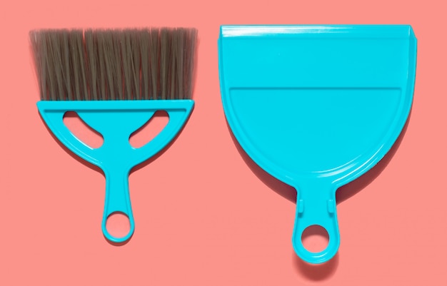 A pale blue dustpan and brush lying on living coral color. Top view. 