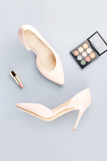 Pale pink female shoes, lipstick and eyeshadow palette on grey background. Fashion blogger concept flat lay.