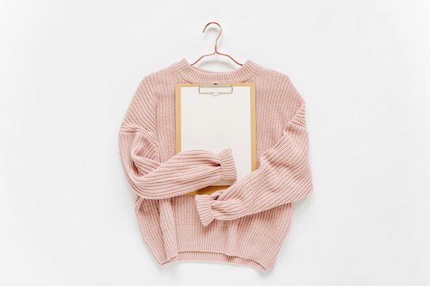 흰색 바탕에 클립보드가 있는 옅은 분홍색 니트 스웨터. 가을과 겨울 옷. 상점, 판매, 패션 컨셉입니다.