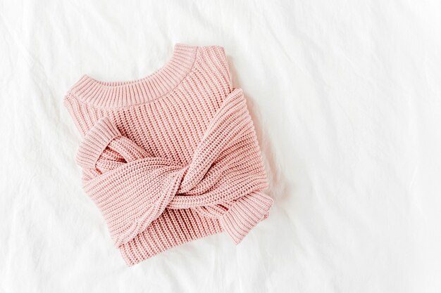 Pale pink warm sweater  on bed. Women's stylish autumn or winter clothes. Cozy Winter look.  Flat lay, top view.