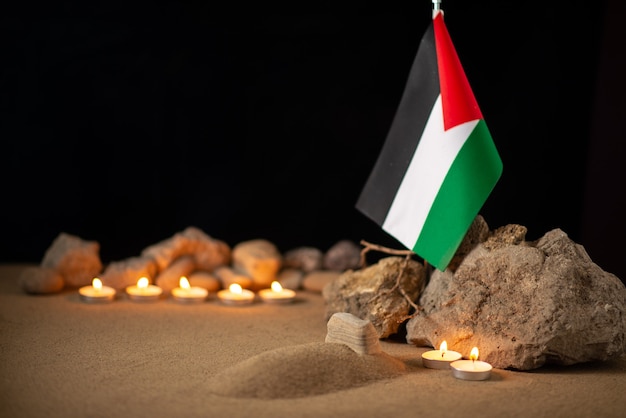 Palestinian flag with stones and burning candles on dark surface