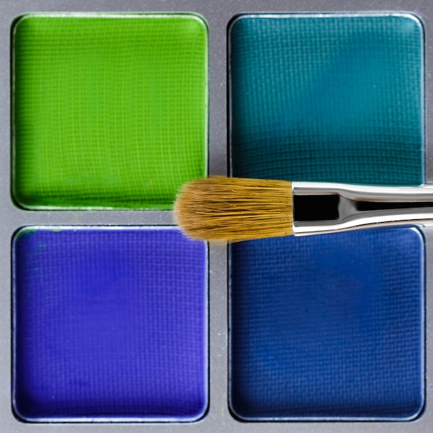 Palette of blue and green eye shadow and makeup brush