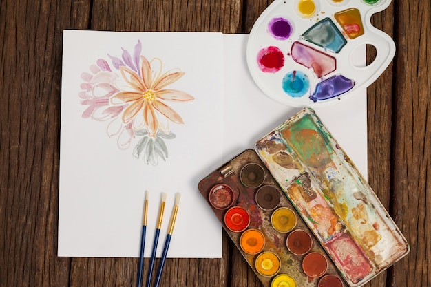 Palette, paint brushes and white sheet on wooden table