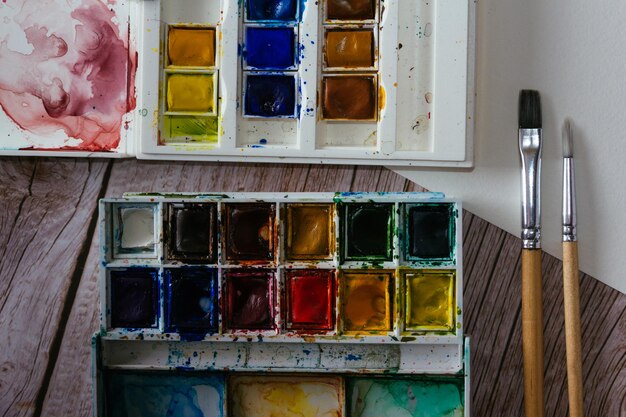 palette of watercolor paints blank paper and brushes on wooden background artist's work space