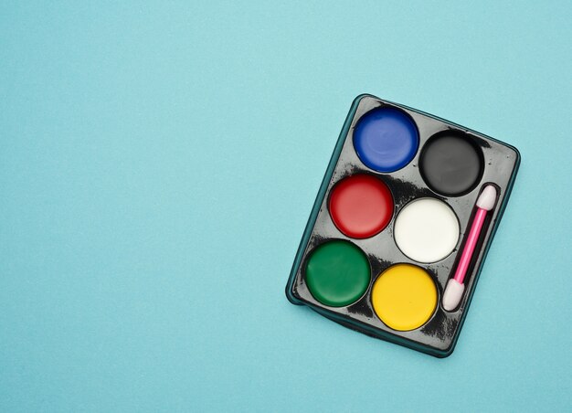 Palette with multi-colored makeup paints on a blue