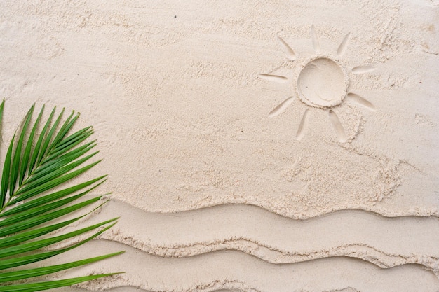 A palm leaf is in the sand and the sun is drawn in the sand.