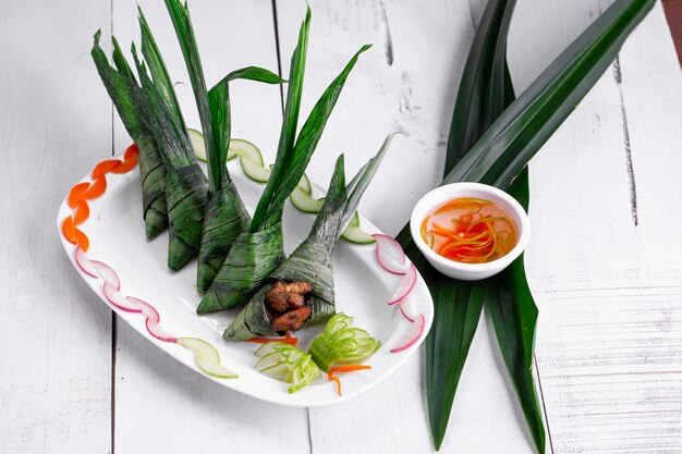 Palm leaf wrapped chicken placed beautifully in a white ceramic plate