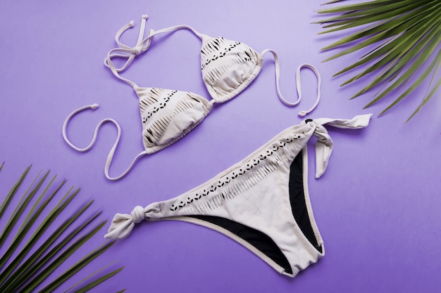 Photo palm leaves and bikini on violet or purple surface, travel and vacations concept, top view