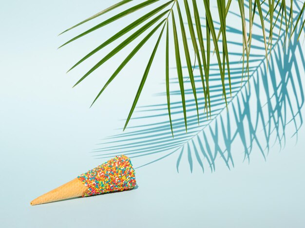 Palm tree leaf and colorful ice cream cone on pastel blue background summer tropical concept