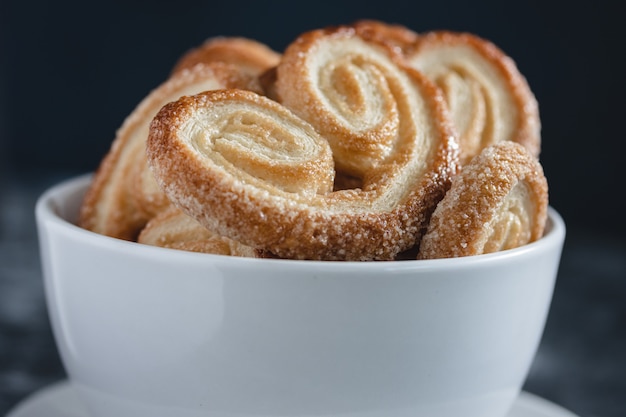 Palmier Puff Pastry. Delicious french palmier cookies with sugar in a white bowl on dark surface