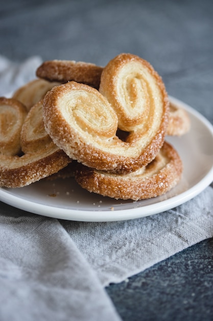 Palmier Слоеное тесто. Вкусные французские ладонь печенье с сахаром на белой тарелке на темной поверхности