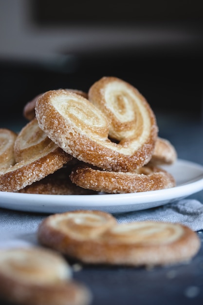 Palmier Слоеное тесто. Вкусные французские ладонь печенье с сахаром на белой тарелке на темной поверхности