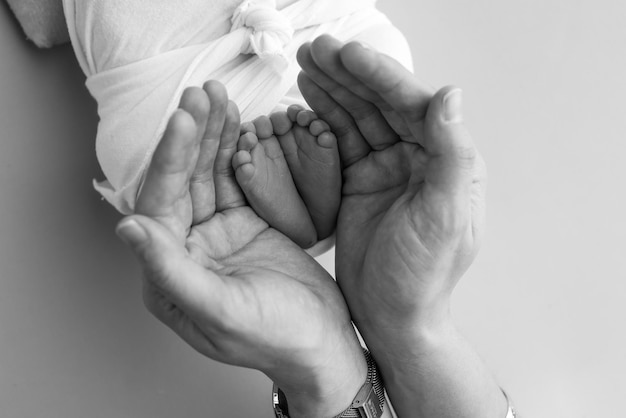 The palms of the father the mother are holding the foot of the newborn baby Feet of the newborn on the palms of the parents Photography of a child's toes heels and feet Black and white macro